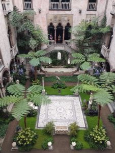 A view of the garden inside the Isabella Stewart Gardner Museum. It looks like a courtyard with symmetrical plantings of trees, flowers, and groundcover.