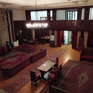 A view overlooking the great hall, which includes wood paneled walls, large couches, some tables, and large stately rugs