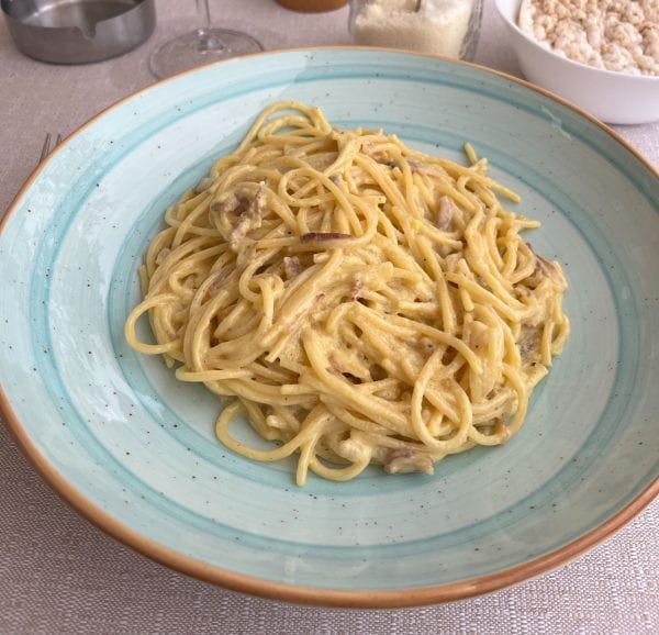 A heaping bowl of spaghetti carbonara in a stylish light blue plate.