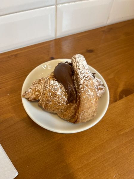 A small croissant overflowing with nutella stuffing sitting on a small dish.