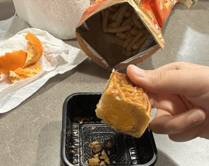 A mooncake being held over a take-out container
