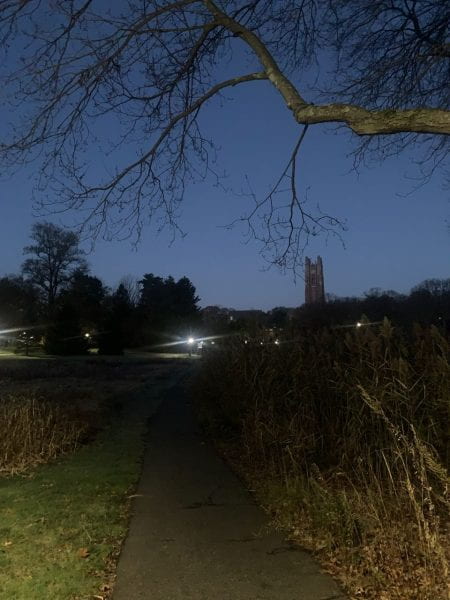 Galen Stone Tower and other parts of campus illuminated by streetlights under a navy sky slowly brightened by sunrise.