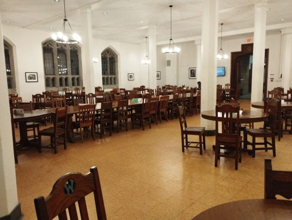 Image of tables and chairs with hanging lights and ornate windows in a dining hall.