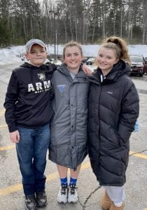 Image of Anna and her brother and sister standing in a parking lot after a game. 