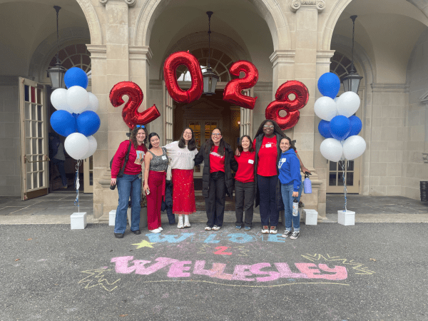 Jade and other students standing in front of a display of balloons reading "2028" and a chalk drawing saying "Welcome 2 Wellesley"