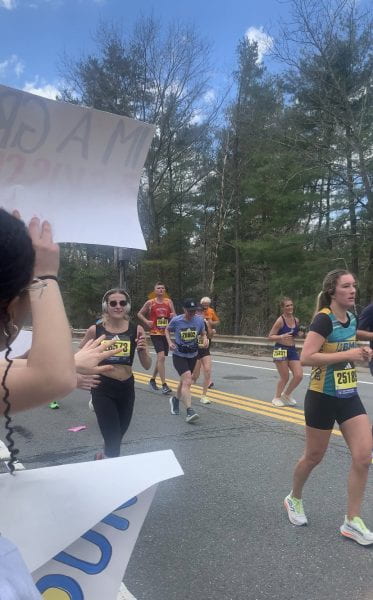 Image of Boston Marathon runners alongside Wellesley students holding signs.