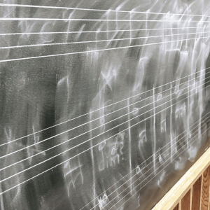 Image of musizcal notation partially erased on a chalkboard.